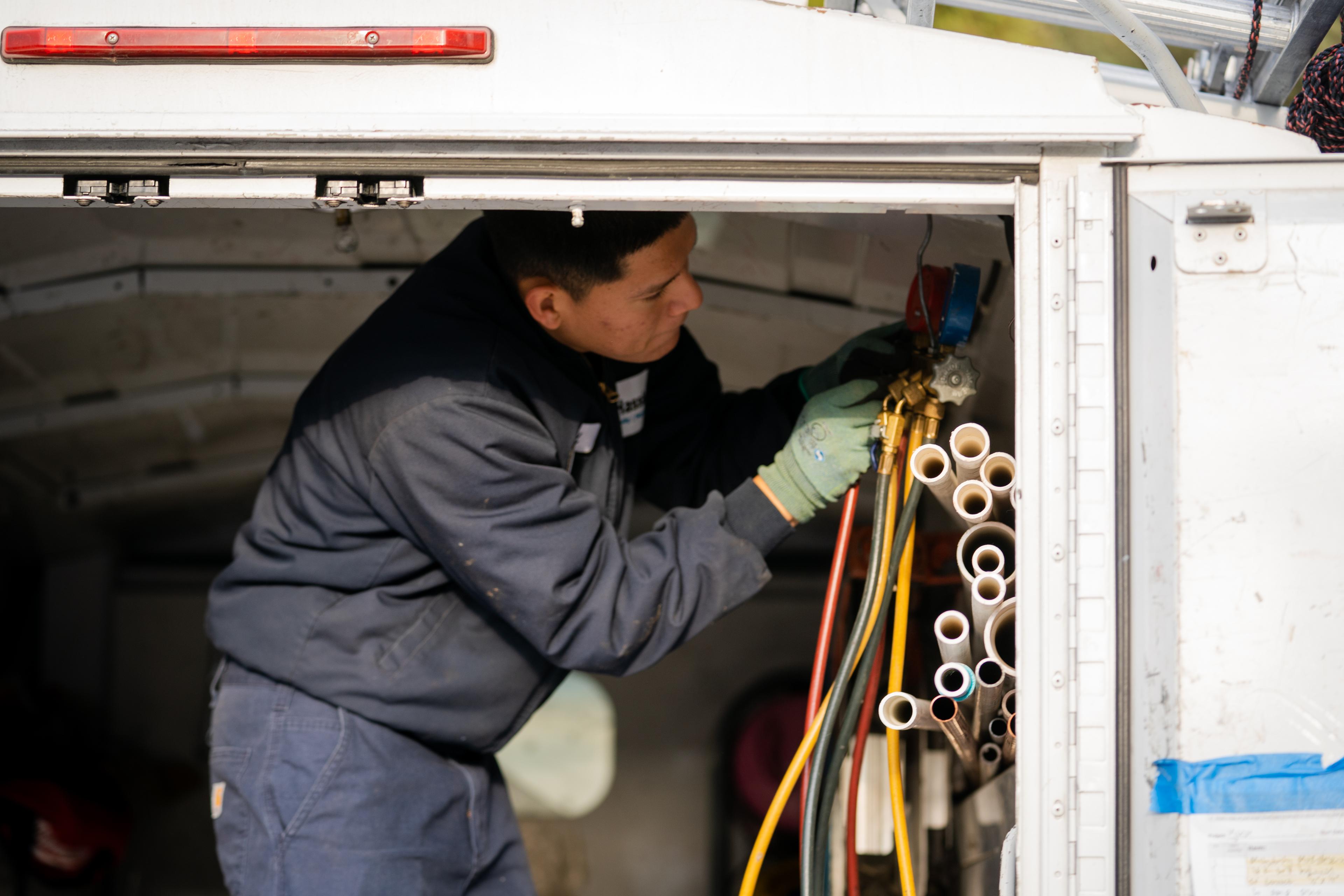 Picture of A Hassler technician works on a client's HVAC system. - Hassler Heating & Air Conditioning, LLC