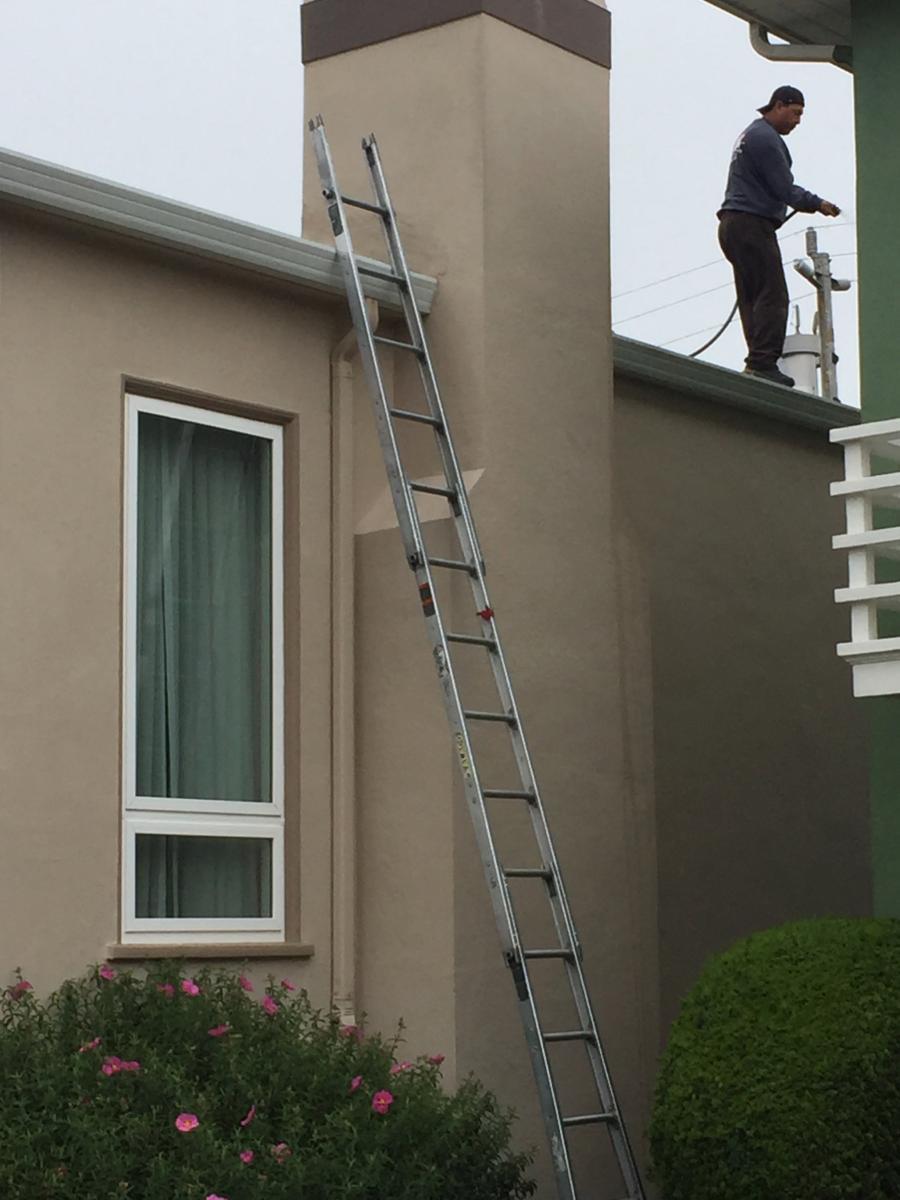 Picture of AWC technician Eduardo rinses gutters to make sure the downspouts are functioning properly. - AWC