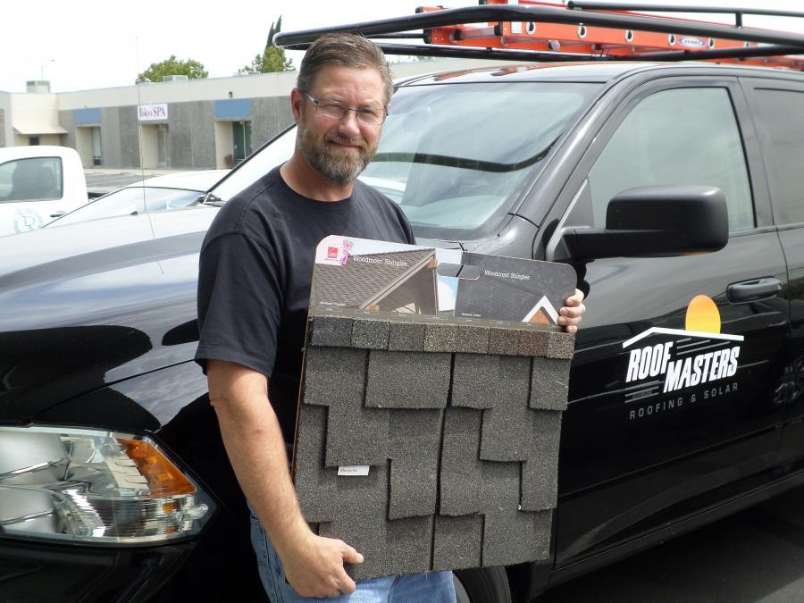 Picture of Owner Aaron Weiss holds a roofing sample in front of one of his service trucks. - Roofmasters of California LLC