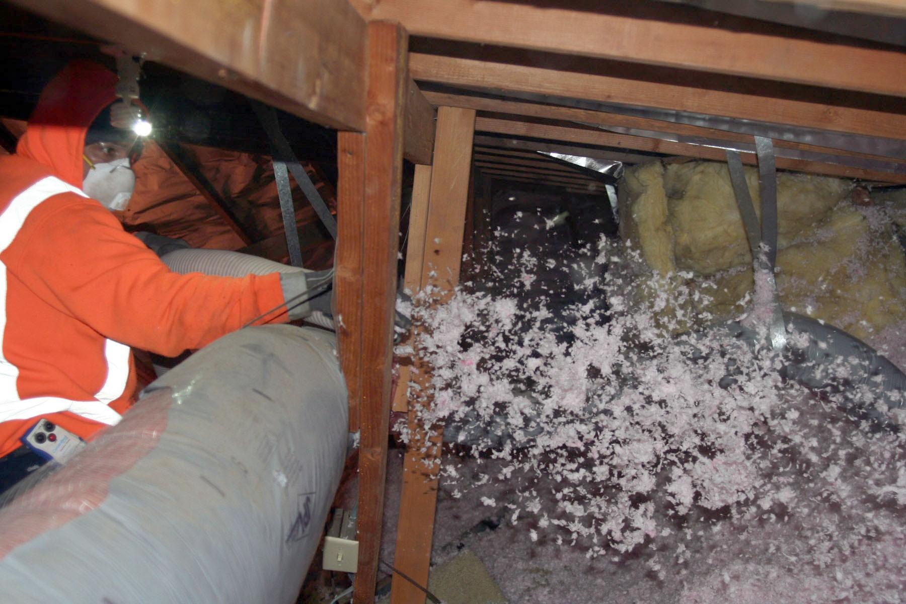 Picture of An Alcal Specialty Contracting employee installs Owens Corning L77 loose-fill insulation in an attic. - Alcal Specialty Contracting, Inc.