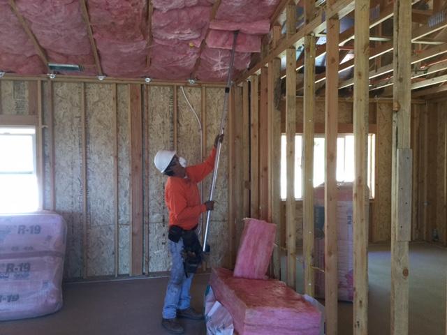 Picture of An Alcal Specialty Contracting employee installs batt insulation between floors in a new home. - Alcal Specialty Contracting, Inc.