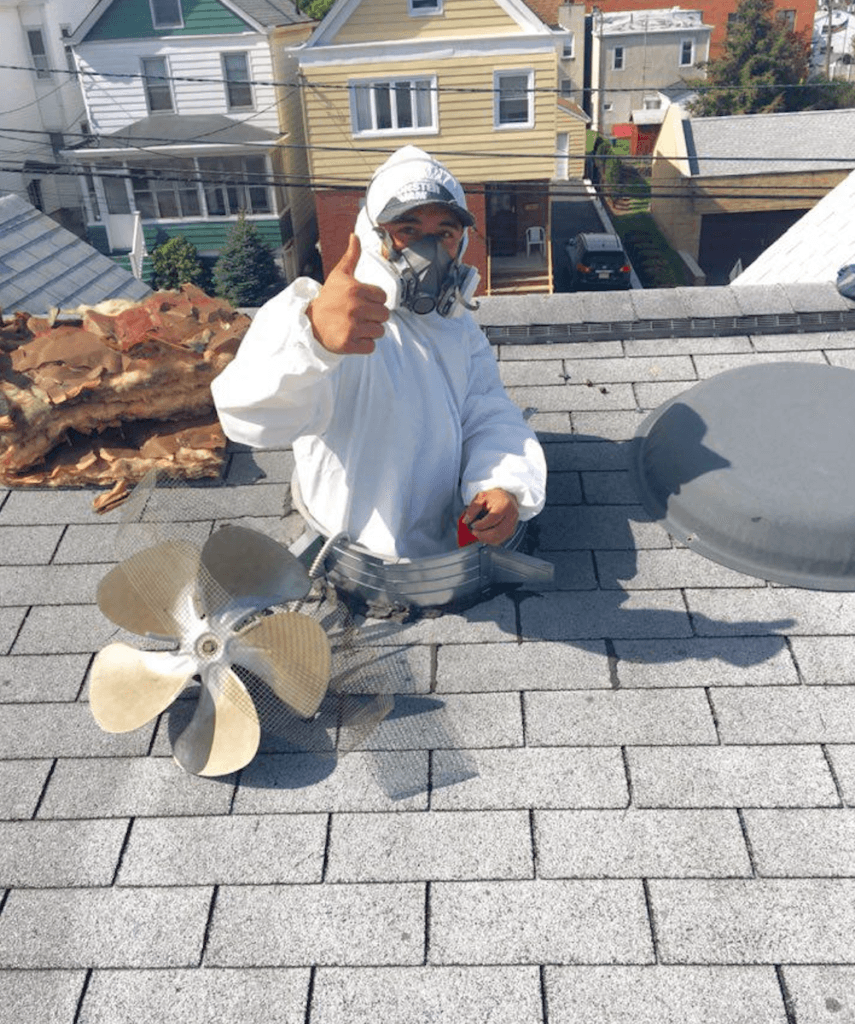 Picture of An Atticare technician poses on a client's roof while working on the attic underneath. - Atticare Construction