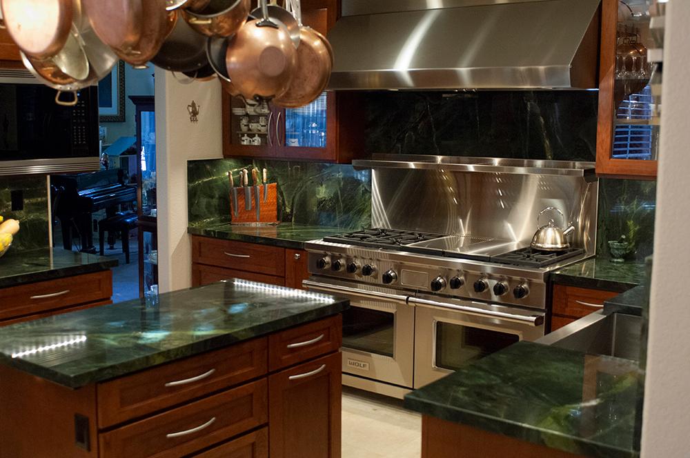 Picture of The centerpiece for this total room transformation is a 60-inch Wolf gas range with a custom vent hood. The next eye-catching aspect of this kitchen is a green Vitoria Regia Granite countertop and backsplash. - Cook's Kitchen & Bath, Inc.