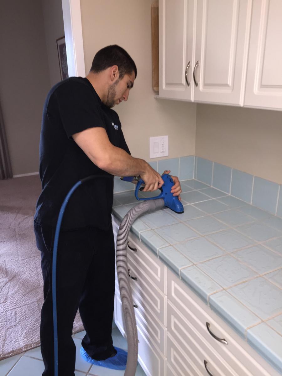 Picture of Brandon Steely cleans a customer's kitchen tile. - Maximum Carpet Cleaning