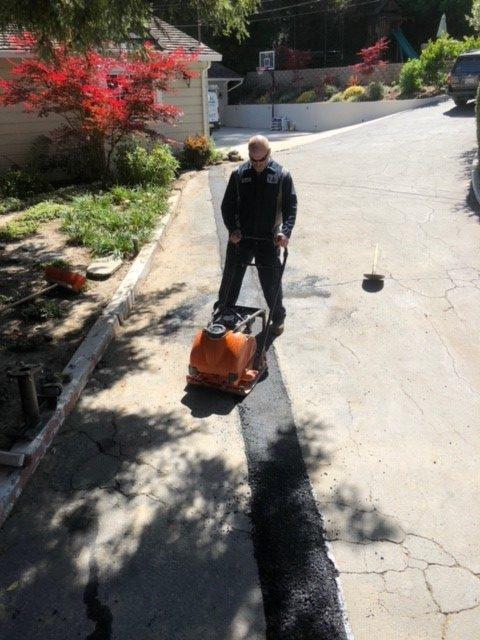 Picture of An Absolute Plumbing and Drain technician installs an asphalt patch in a client's driveway. - Absolute Plumbing and Drain
