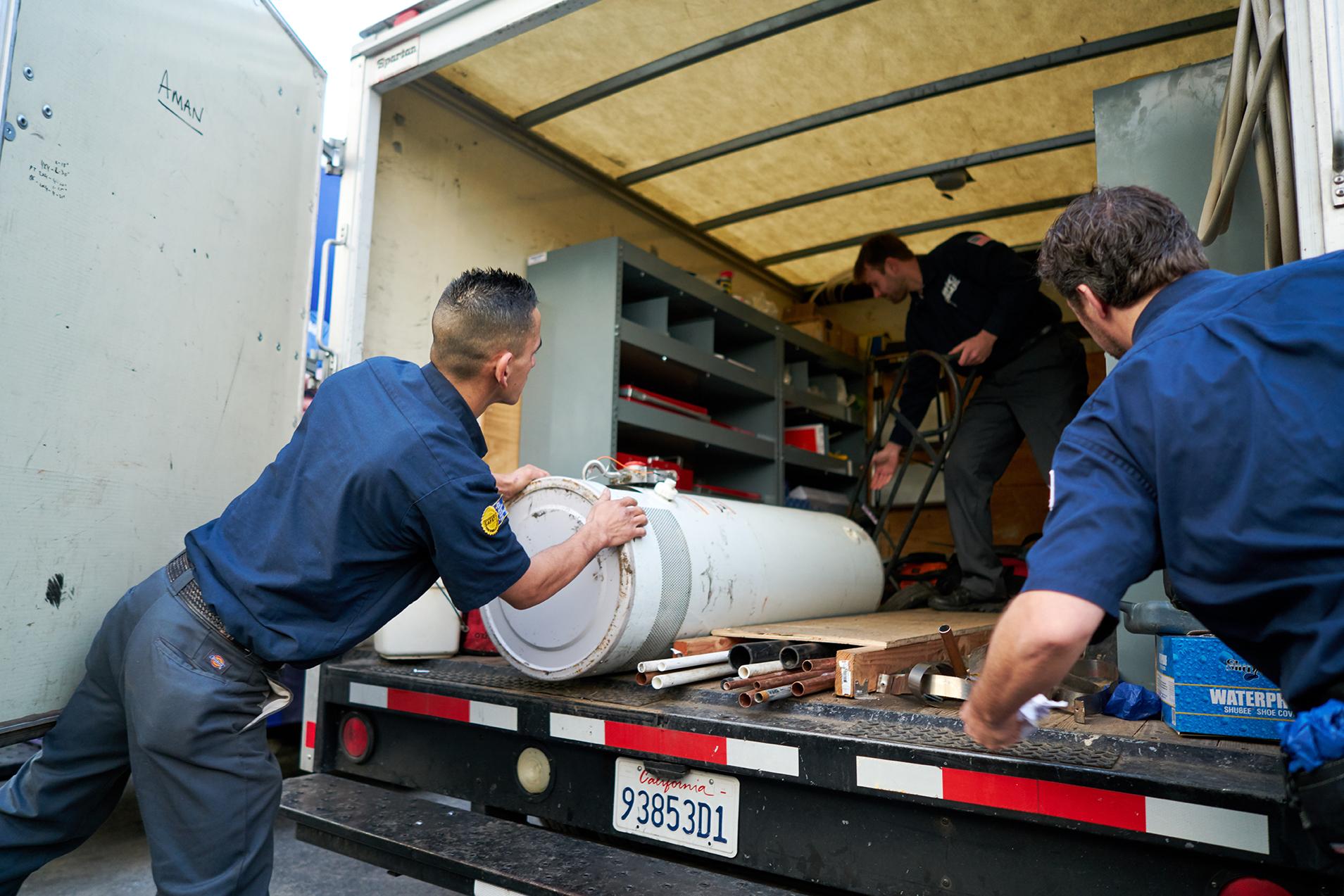 Picture of Three Big Blue Plumbing technicians unload a truck on a recent jobsite. - Big Blue Plumbing