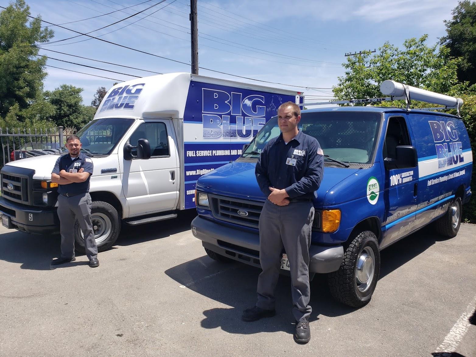 Picture of Two Big Blue Plumbing technicians stand next to their service trucks. - Big Blue Plumbing
