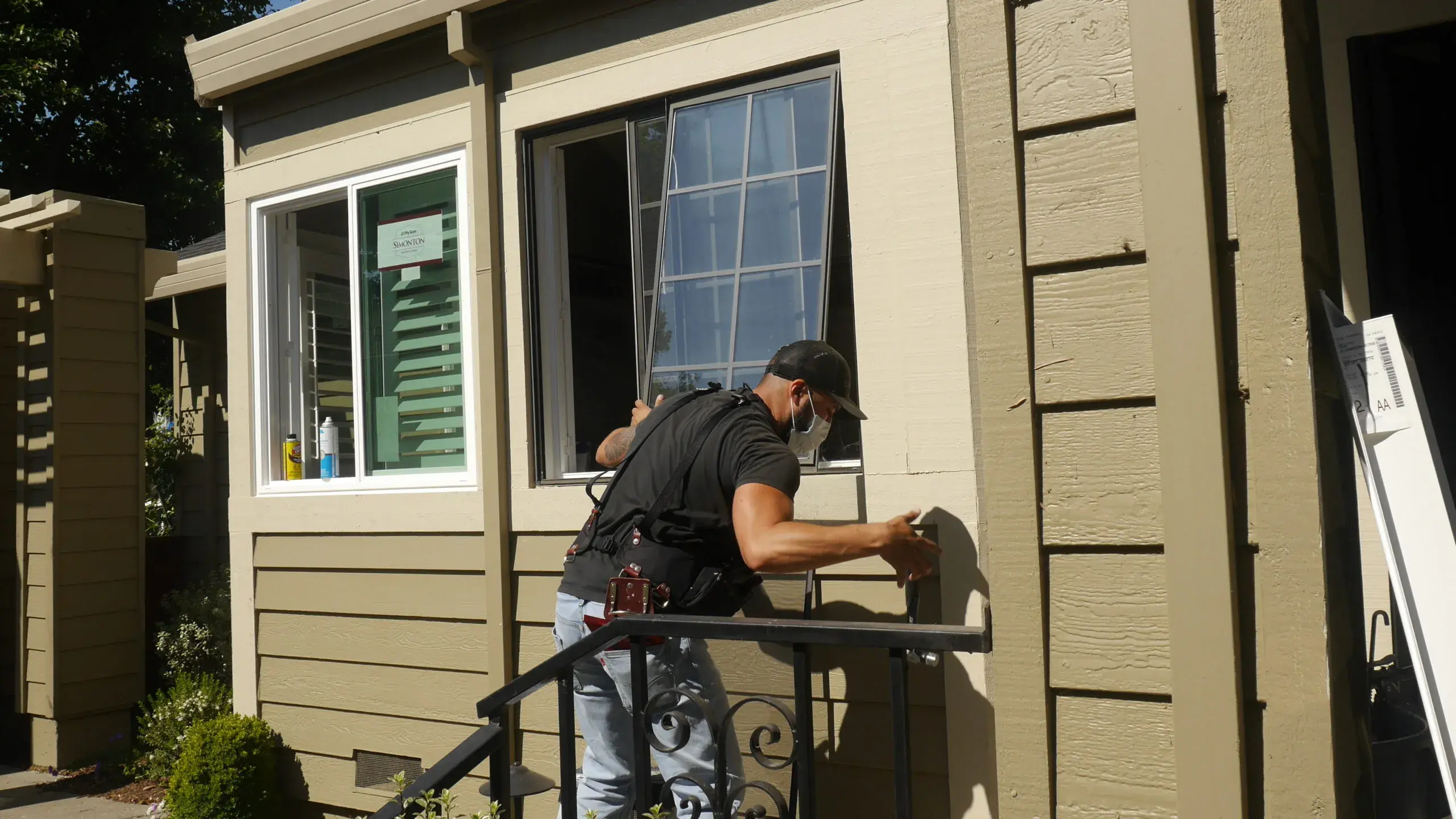 Picture of Master Installer Eduardo Jr. carefully removes a sliding pane of glass from an existing window. To his left is the new replacement window he just installed. - Save Energy Company