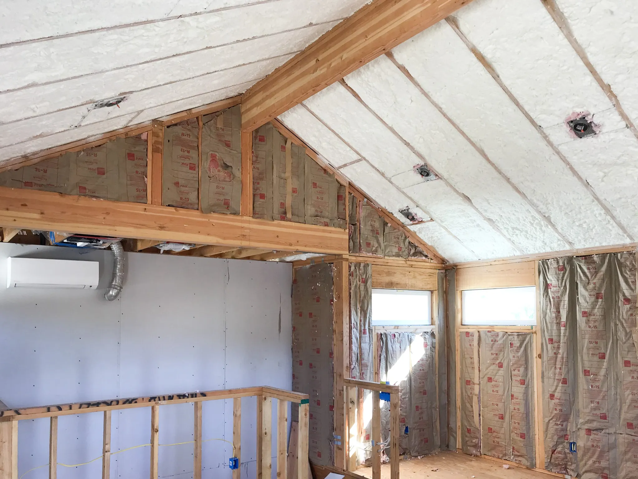  A room with vaulted ceilings shows installed insulation. Exposed wooden beams and partially finished walls surround the space, highlighting ongoing construction work.