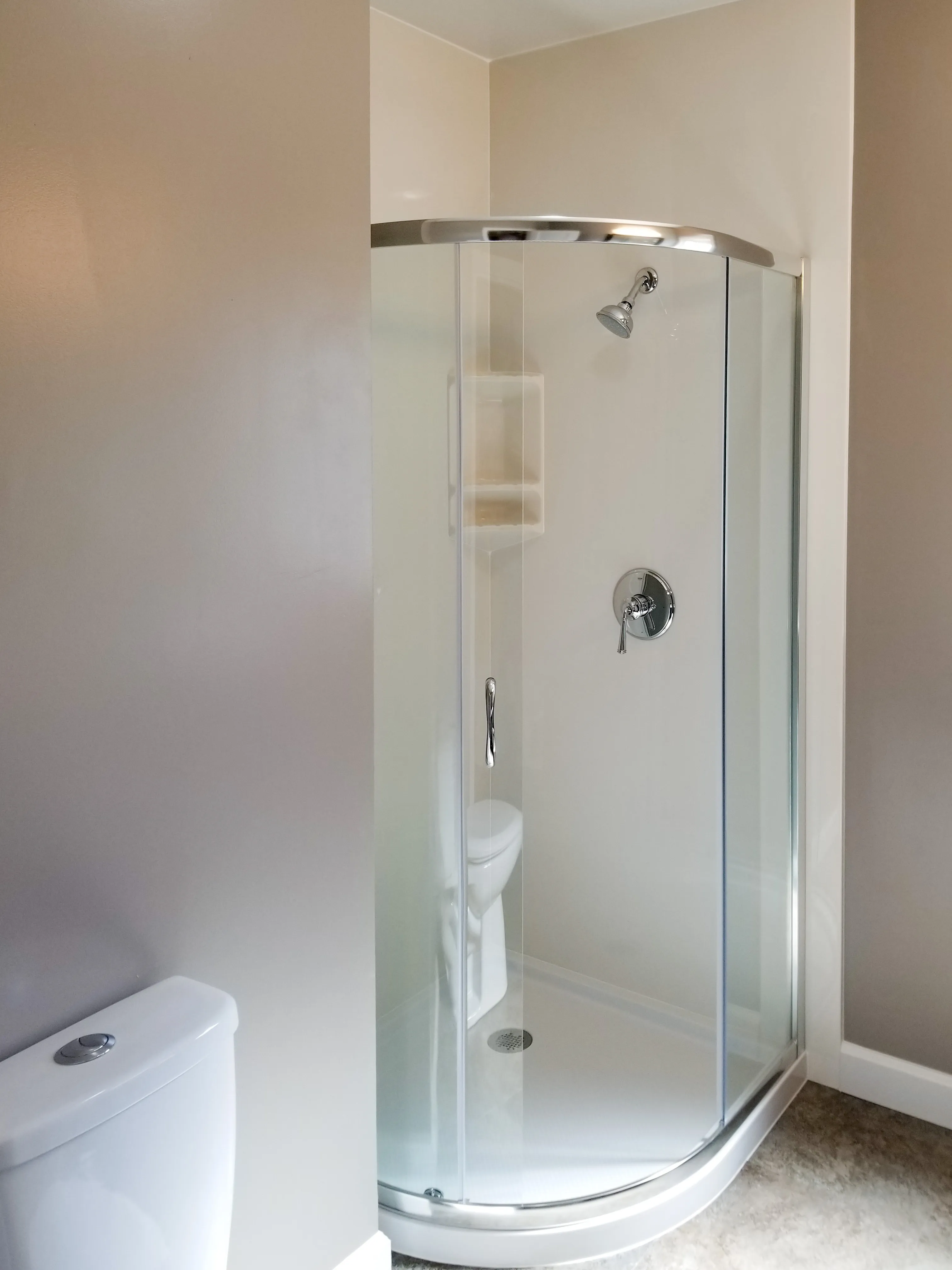 A modern bathroom features a curved glass shower enclosure next to a white toilet, set against beige walls. A modern bathroom features a curved glass shower enclosure next to a white toilet, set against beige walls.