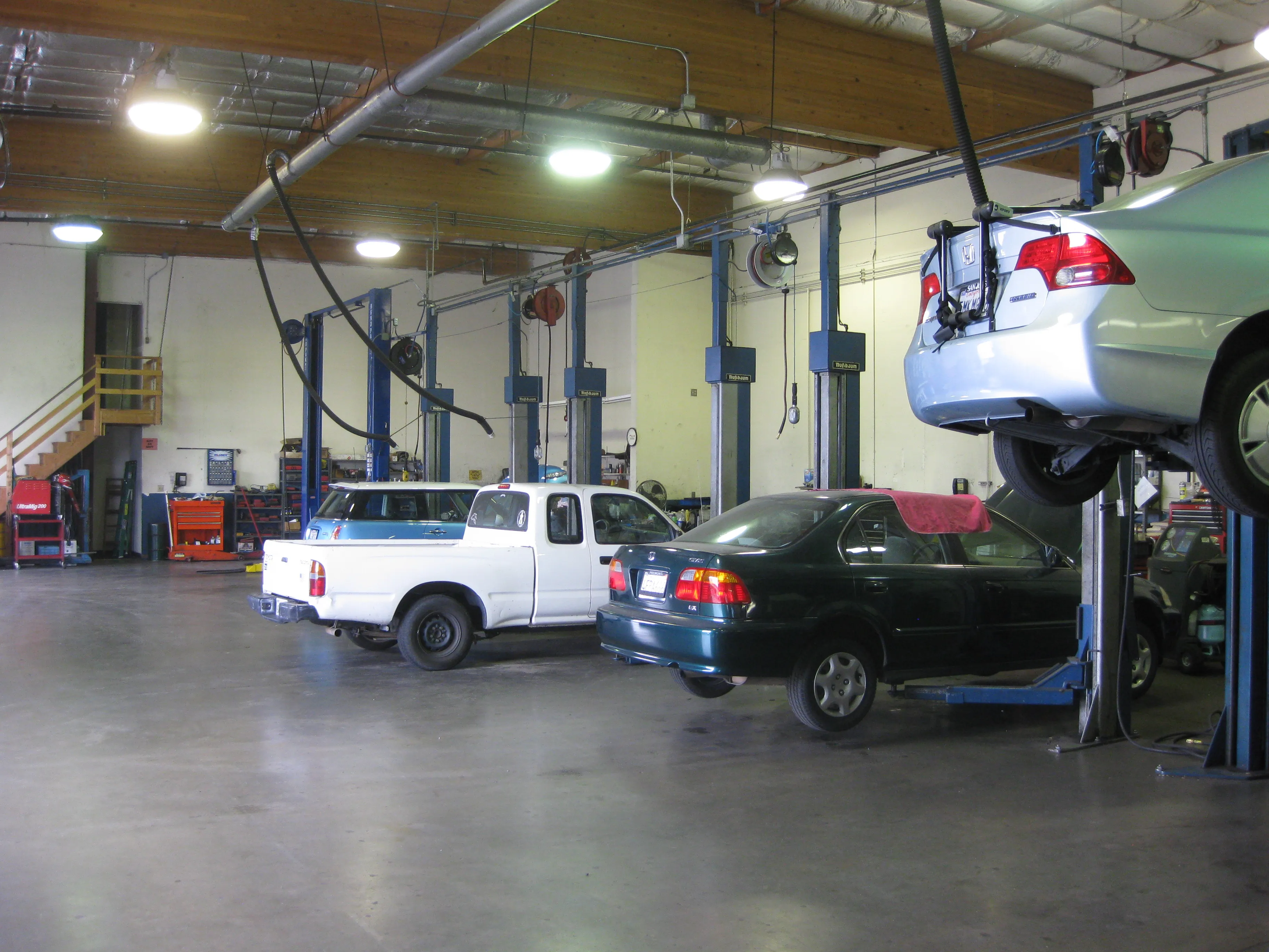 Auto repair shop with cars on lifts, a white truck, and a dark sedan. Tools and equipment are organized along the walls. Bright lighting and clean floors visible.
Auto repair shop with cars on lifts, a white truck, and a dark sedan. Tools and equipment are organized along the walls. Bright lighting and clean floors visible.