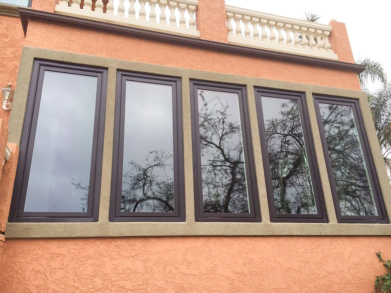 Picture of A row of sleek, dark-framed windows reflects the intricate silhouettes of leafless trees against a peach stucco wall. This installation by Abstract Windows highlights the companyâ€™s focus on quality outcomes, ensuring elegance and durability for every home. Copyright ©2025 Diamond Certified Resource

 - Abstract Windows