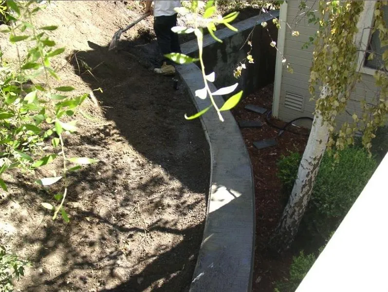 Picture of A worker meticulously shapes the earth against a newly constructed curved retaining wall, blending functionality with the natural landscape. Engineered Soil Repairs, Inc. excels in creating quality outcomes. Copyright ©2025 Diamond Certified Resource. - Engineered Soil Repairs, Inc.