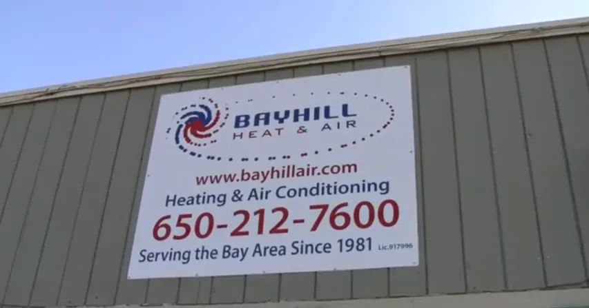 A large sign on a building reads "Bayhill Heat & Air," displaying the company website, phone number, and service area since 1981.
