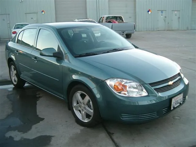 A clean, green Chevrolet sedan is parked on a concrete surface in front of large industrial garage doors.