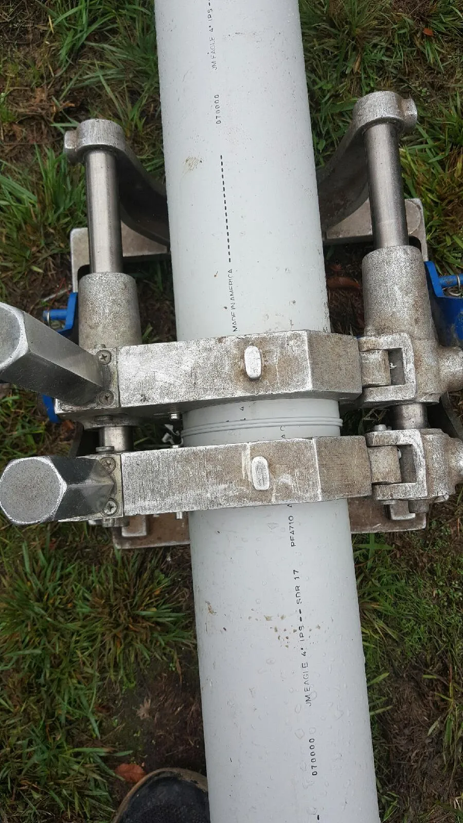  Close-up of a metal clamp holding a large white pipe on grassy ground.