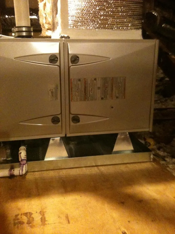  A close-up of a furnace unit installed on a wooden platform with metal venting and insulated surroundings.