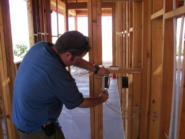  Person in a blue shirt working on electrical wiring within a wooden framed structure. Tools are visible.