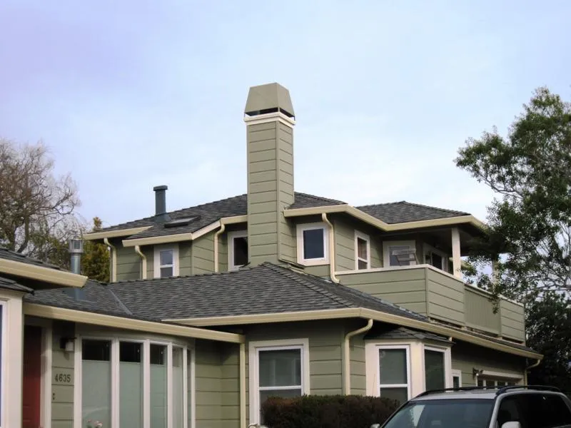 A house with a green exterior and multi-story design featuring a prominent chimney and well-maintained shingle roofs. A house with a green exterior and multi-story design featuring a prominent chimney and well-maintained shingle roofs.