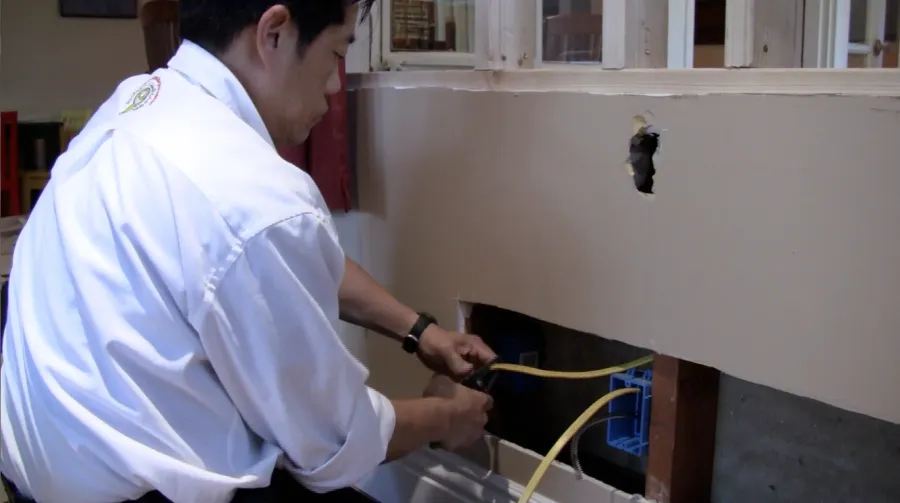 Picture of  A technician from Aren Electric Co., Inc. meticulously works on wiring inside a wall cavity, showcasing the company's focus on quality outcomes. Aren Electric Co., Inc. is recognized for expertise and quality. Copyright ©2025 Diamond Certified Resource.

 - Aren Electric Co., Inc.