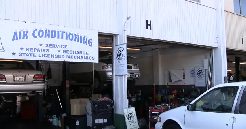  Auto repair shop with cars lifted on hoists, tools, and equipment. Sign reads "Air Conditioning Service Repairs Recharge State Licensed Mechanics."