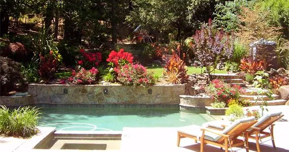 A beautifully landscaped backyard with a swimming pool, lush greenery, colorful flowers, and stone patio with lounge chairs.