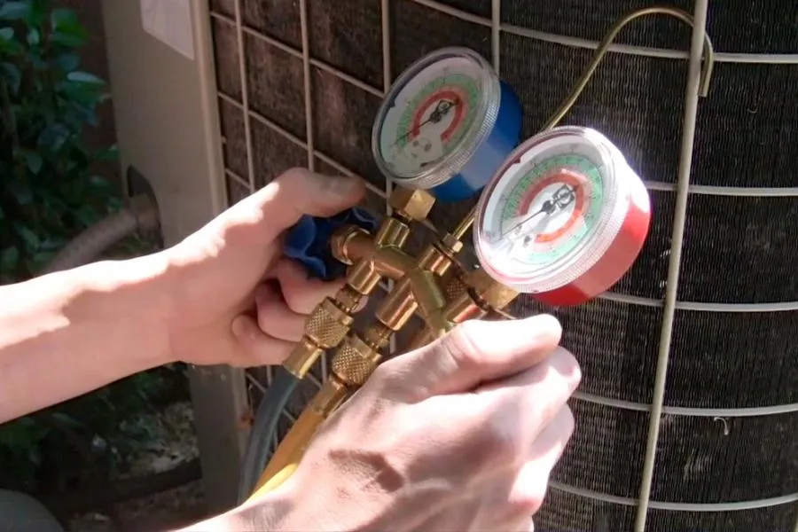 Hands adjusting pressure gauges on an HVAC unit outside, with greenery in the background.
