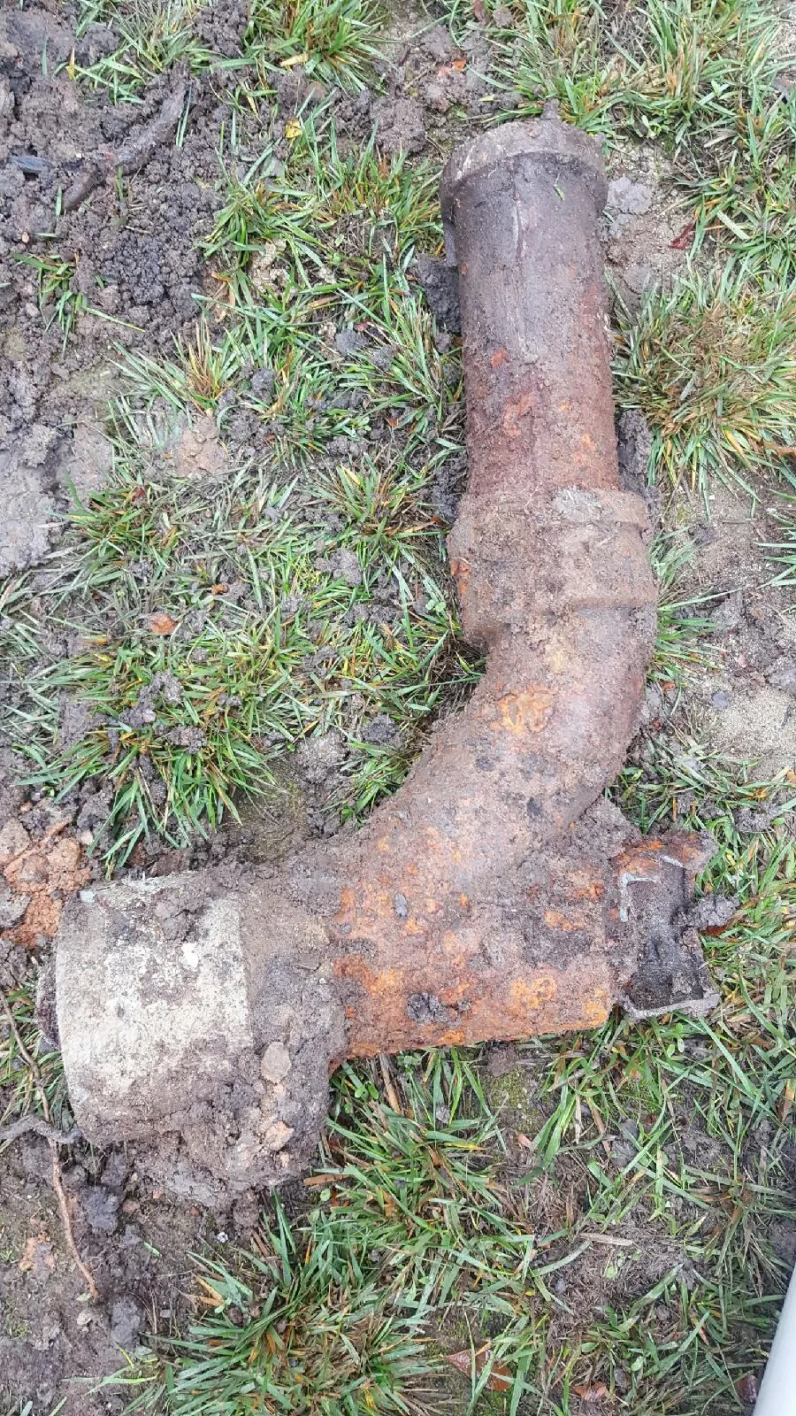  Rusty and corroded pipe lying on grass, partially covered with soil and dirt.