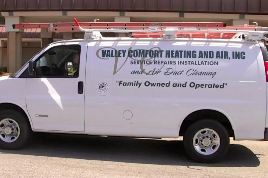  White Valley Comfort Heating and Air van with company logo, parked outside a building with a ladder on its roof.