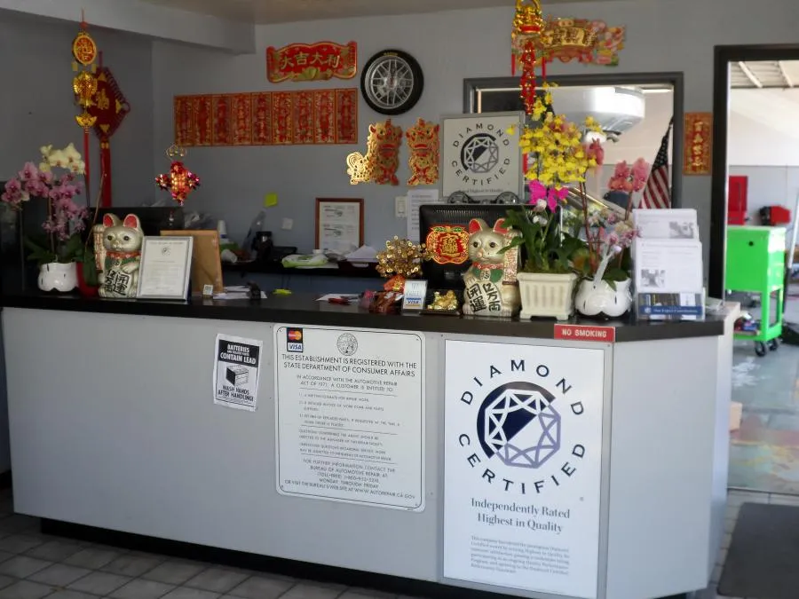  A reception counter with colorful decorations, including plants and lucky cat figurines, displays a Diamond Certified sign and various documents and notices.
