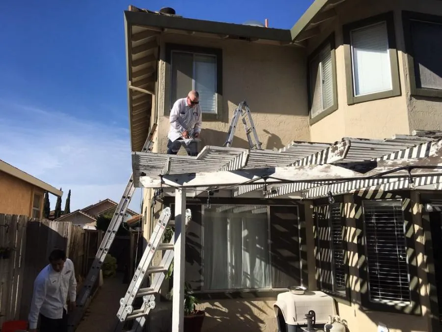  Two technicians on ladders inspect a home's roof under a clear blue sky.