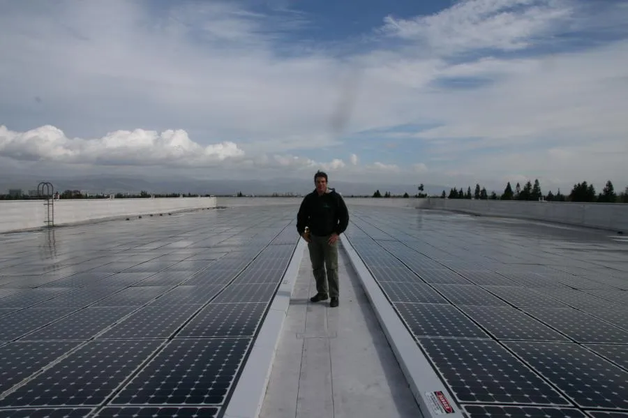  A person stands on a rooftop surrounded by an extensive array of solar panels under a cloudy sky.