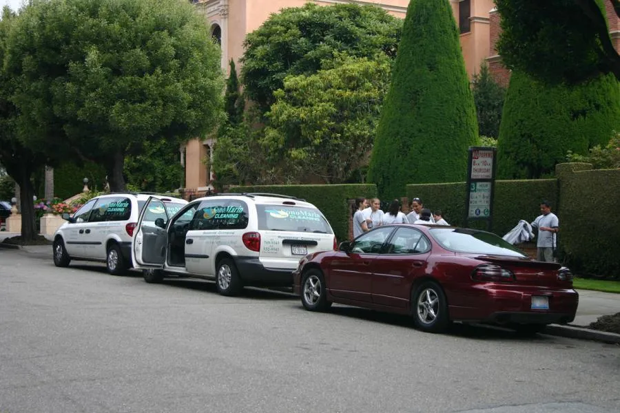  Two SonoMarin Cleaning Services vans parked on a residential street with people gathered nearby, preparing for work.