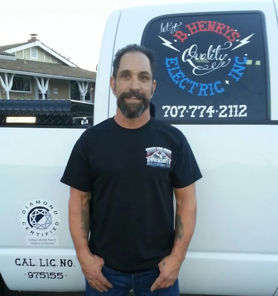  Person in a black shirt standing beside a white B. Henry's Quality Electric Inc. vehicle with company branding and Diamond Certified logo.