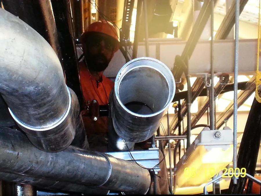  Worker in orange attire inspecting industrial pipes with structural beams and scaffolding in the background.