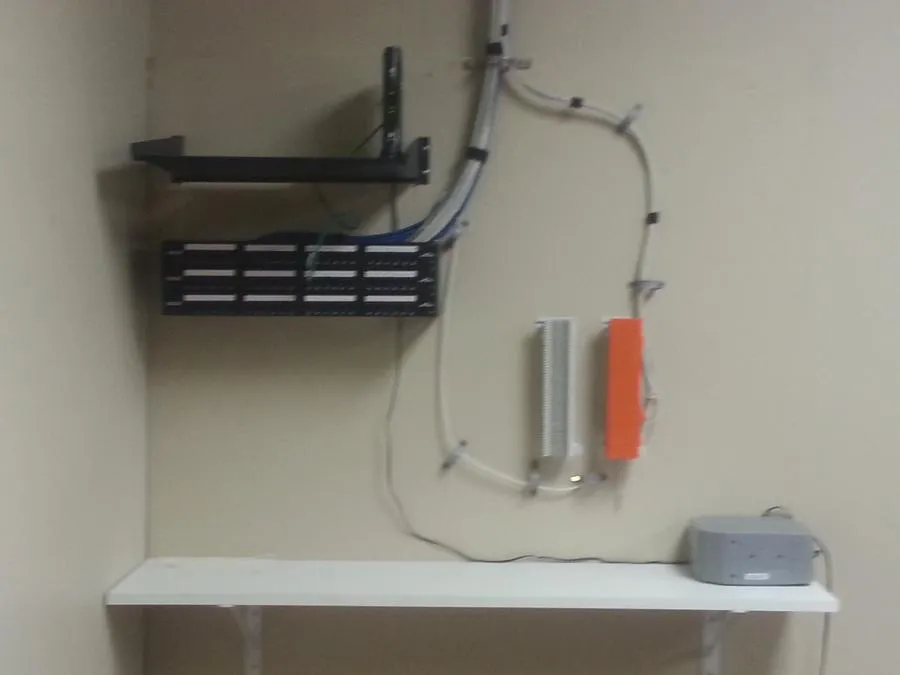 A wall-mounted network setup with organized cables, equipment on shelves, and a small device on a lower shelf.
