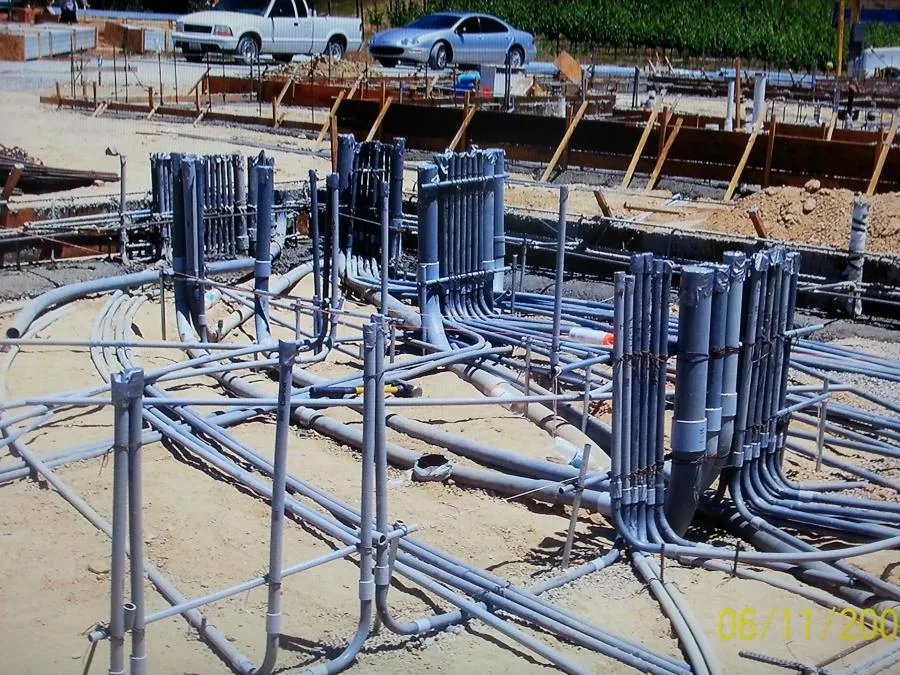  Construction site with exposed electrical conduits and wires arranged on the ground, surrounded by dirt and wooden forms.