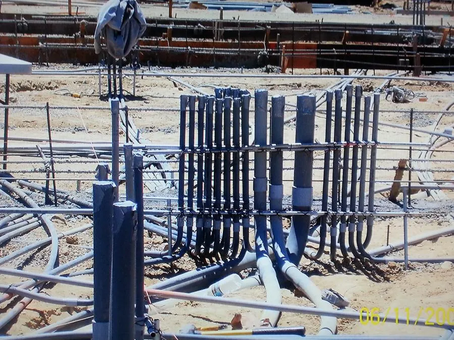  Electrical conduits and pipework intricately arranged at a construction site, with surrounding rebar and unfinished foundations visible.