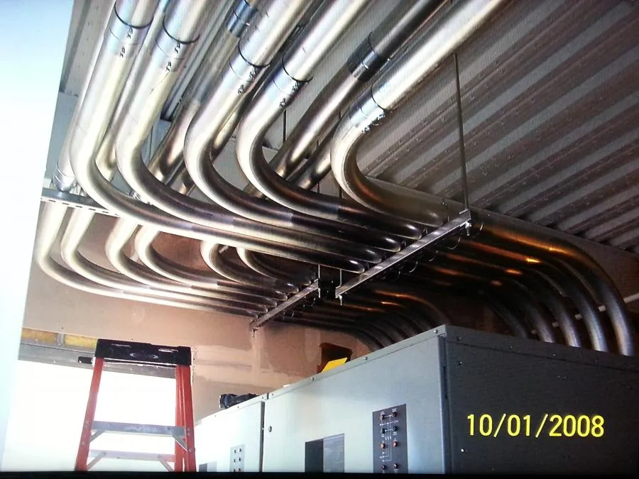  Multiple metal conduits installed along a ceiling, with a red ladder and electrical panel visible below.