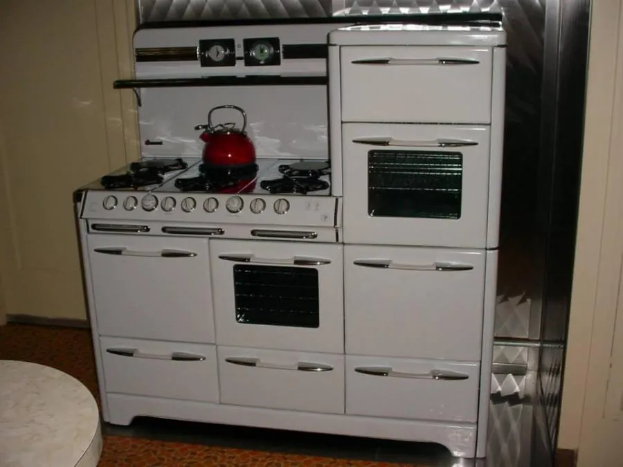Picture of A classic white stove with a vivid red kettle rests in a kitchen, embodying timeless design and reliability. Bell Products, Inc. is recognized for expertise and quality in creating such enduring kitchen essentials. Copyright ©2025 Diamond Certified Resource. - Bell Products, Inc.