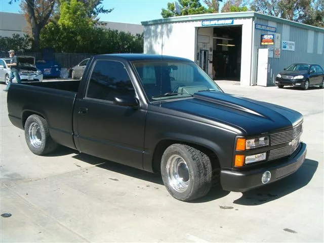  A black pickup truck with a smooth finish is parked in front of an auto repair shop. The shop has signs with "Coelho's Body Repair & Auto Sales, Inc." visible in the background.