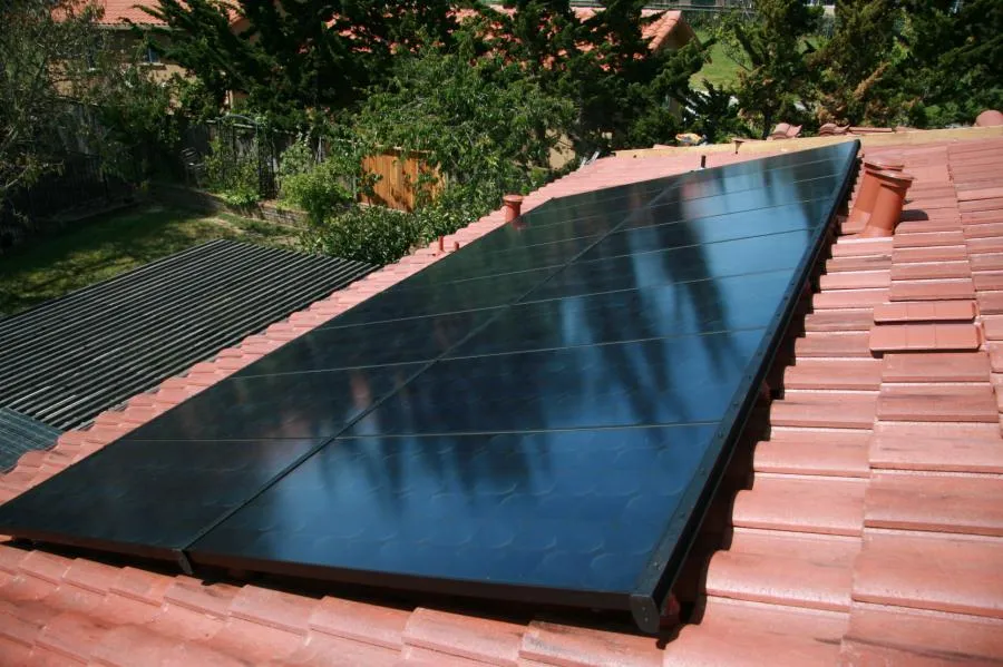 Solar panels installed on a red-tiled roof, surrounded by trees and garden area in the background.