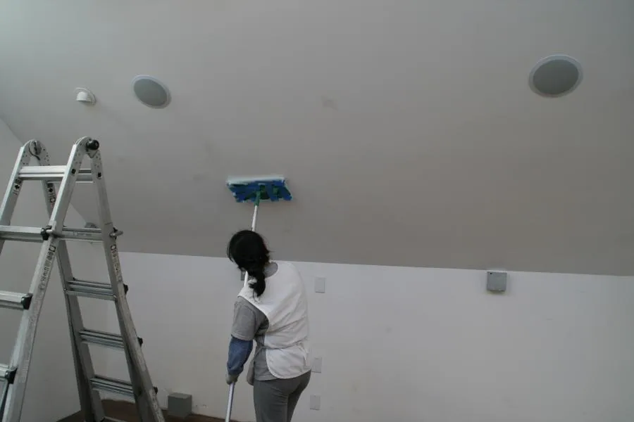 Person cleaning a sloped ceiling with a mop next to a ladder, wearing a white and gray outfit.