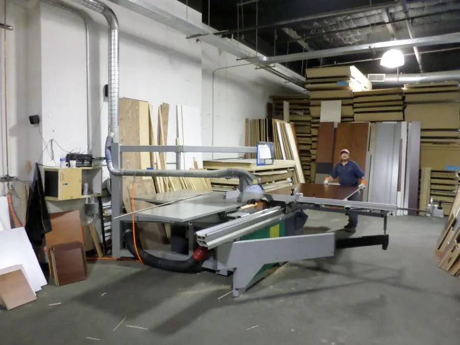 Picture of In a well-organized workshop, a craftsman expertly manages a large cutting machine, surrounded by neatly stacked wood panels, exemplifying Closet Factoryâ€™s focus on quality outcomes. Copyright ©2025 Diamond Certified Resource - Closet Factory