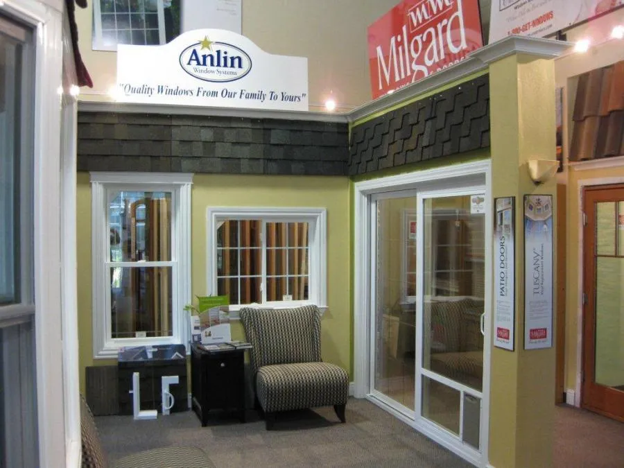 Showroom display of windows and sliding doors with patterned chairs in front. Anlin and Milgard signs are visible above. Showroom display of windows and sliding doors with patterned chairs in front. Anlin and Milgard signs are visible above.