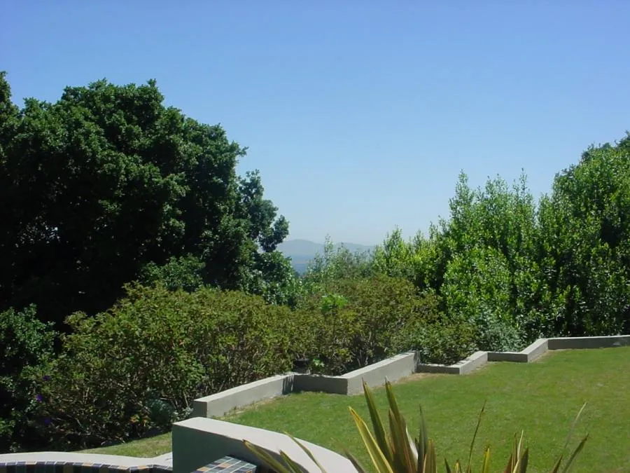  Landscaped garden with neatly trimmed hedges, lush trees, and a well-maintained lawn under a clear blue sky.