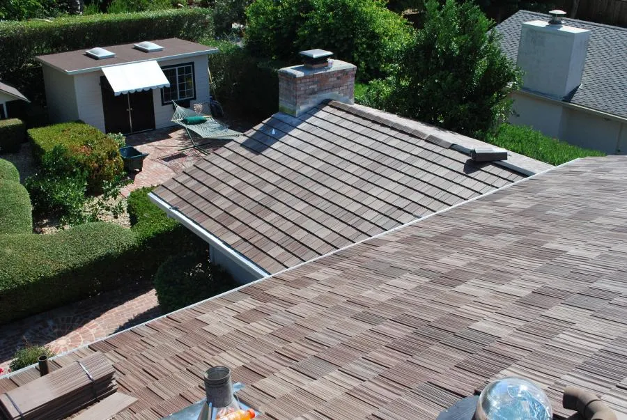  View of a freshly installed roof with timber shingles, adjacent to a garden with a shed and hammock.