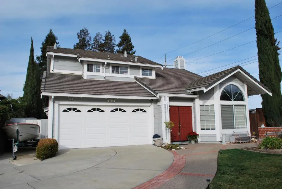  A two-story house with a well-maintained roof, large garage doors, red front doors, and a boat parked in the driveway.