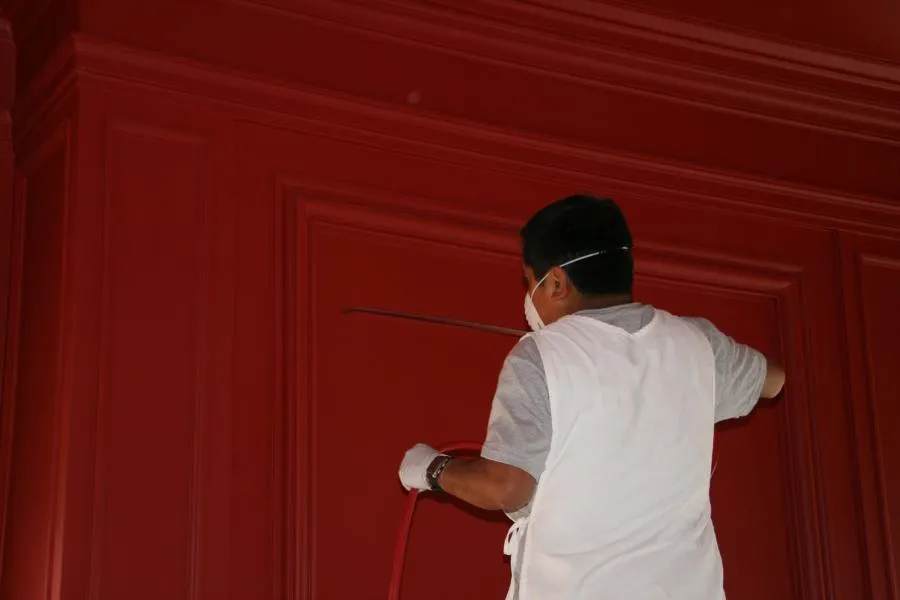  Person in a mask and gloves painting red paneling with a brush, ensuring smooth coverage on the surface.