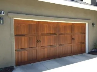  A wooden garage door with decorative handles set into a garage frame against a beige wall.